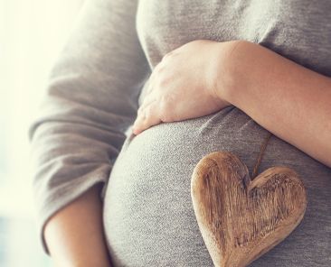 Young pregnant woman holds wooden heart. Love concept. Pastel toning